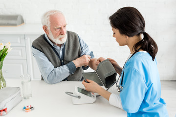 Wall Mural - Nurse measuring blood pressure of bearded grey haired man