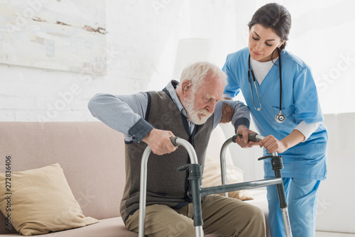 Cuadros en Lienzo Doctor helping to retired man, getting up from sofa