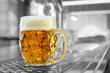 Freshly poured draft lager beer in a dimpled glass mug on stainless steel counter in a modern pub. Black and white background. Space for text.
