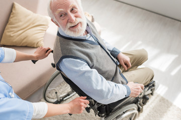 Wall Mural - High angle view of disabled and cheerful gray haired man in wheelchair looking at nurse