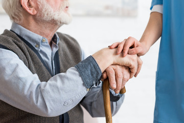 Wall Mural - Cropped view of nurse holding hands with bearded senior man