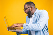 © denis_vermenko - Young surprised african american man standing and using laptop computer isolated over yellow background.