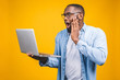 © denis_vermenko - Young surprised african man standing and using laptop computer isolated over yellow background.