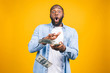 © denis_vermenko - Portrait of a happy young afro american man throwing out money banknotes isolated over yellow background.