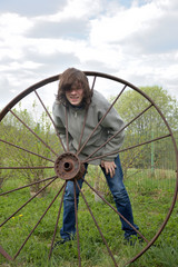 teenage boy having fun playing with an old iron wheel in the countryside