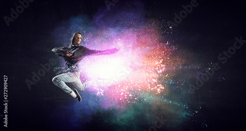 Modern female dancer jumping in hoodie with colourful splashes background. Mi...