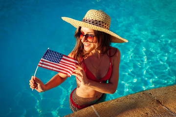 Sexy young woman holding USA flag in swimming pool. Celebrating Independence day of America