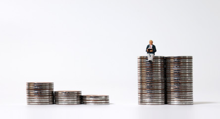 Miniature people sitting on piles of coins.