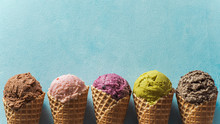 Various Ice Cream Scoops In Cones With Copy Space. Colorful Ice Cream In Cones Chocolate, Strawberry, Blueberry, Pistachio Or Matcha, Biscuits Chocolate Sandwich Cookies On Blue Background. Top View