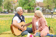 © Pixel-Shot - Mature man playing guitar for his wife in park