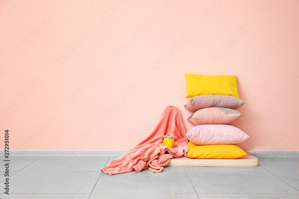 Soft pillows and plaid on floor near color wall