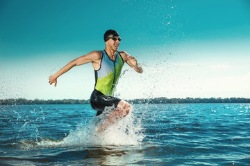 Professional triathlete swimming in river's open water. Man wearing swim equipment practicing triathlon on the beach in summer's day. Concept of healthy lifestyle, sport, action, motion and movement.