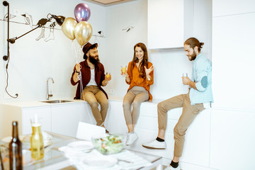 Wall Mural - Young friends having fun during the small birthday party, sitting and having some snacks on the kitchen at home