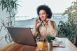 © Mediteraneo - Smiling young African female entrepreneur sitting at a desk in her home office working online with a laptop