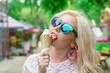 Beautiful, young blonde girl with ice cream in her hands, licks the ice cream on the background of a green park. Italian ice cream in the hands of the girl melted. Close up