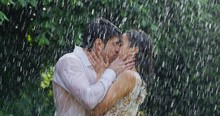 Portrait Of Young Carefree Couple In Love Are Hugging And Kissing Under The Rain On A Background Of Green Trees.