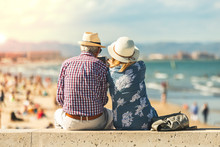 Mature Couple Of Retired Lovers Enjoying Retirement On The Beach Facing The Sea With Mobile Cell Phone Taking Pictures At Sunset. Couple Happy True Love In The Nature