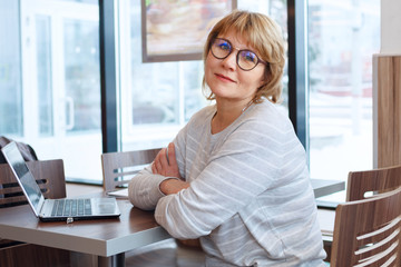 Wall Mural - middle-aged woman business in workplace in cafe, office, she's working on her laptop.