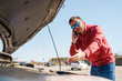 © snedorez - Photo of upset brunet man with phone in next to open hood of broken car in daytime