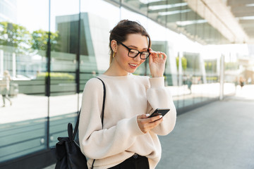 Canvas Print - Photo of cute caucasian woman using cellphone while walking in big city street