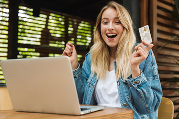 Sticker - Happy young pretty blonde woman in cafe using laptop computer holding credit card.