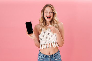 Wall Mural - Happy young woman posing isolated over pink wall background using mobile phone.