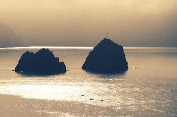 Two rocks and fisher boats in sea at sunrise