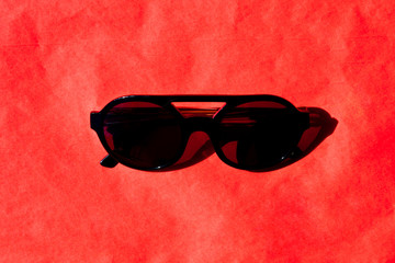 Fashionabls black sunglasses with shadow on red background.