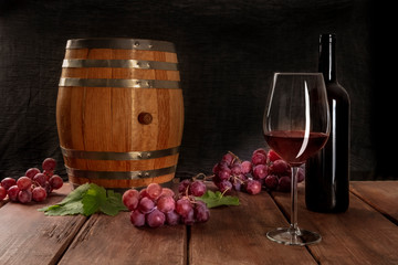 Canvas Print - A glass of red wine with a bottle, a wine barrel, grapes, and vine leaves, on a dark rustic background, low key photo with copy space