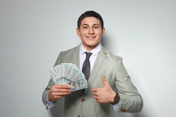 Wall Mural - Portrait of young businessman with money fan on light background