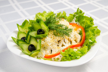 seafood salad - squid, crab sticks, cucumbers, eggs, mayonnaise, cheese, lettuce, tomato, olives and greens on white dish