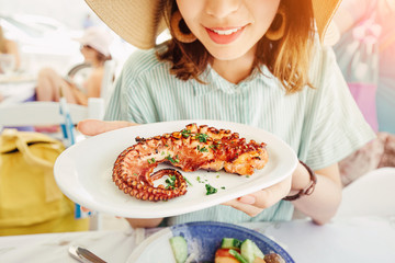 Wall Mural - Happy asian woman in hat eating delicious grilled octopus in seafood restaurant. Delicacy and healthy gourmet cuisine