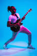 © master1305 - Young african-american musician playing the guitar like a rockstar on blue studio background in neon light. Concept of music, hobby. Joyful attractive guy improvising. Retro colorful portrait.