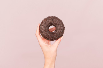 Chocolate glazed donut in hand on a pastel purple background