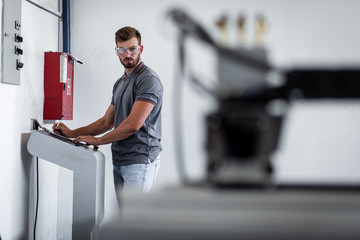 Young engineer setup plasma cutter for work in metalwork workshop.