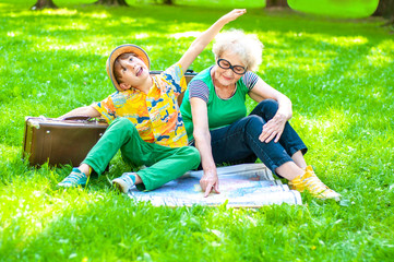 Wall Mural - A trendy grandmother with a grandson of school age and a see map sitting on the lawn with retro suitcases. Concept summer family vacation, travel and tourism. Boy with open hands