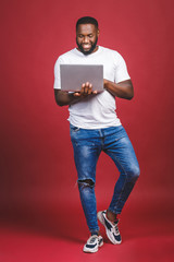 Full length portrait of excited happy afro american man with computer screen and celebrating the win isolated over red background. Thumbs up.