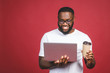 © denis_vermenko - Excited happy afro american man with computer screen, coffee or tea, celebrating the win isolated over red background.