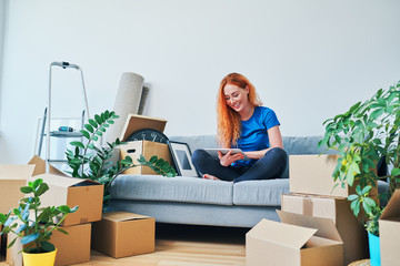 Wall Mural - Beautiful smiling young woman sitting in new apartment and using tablet