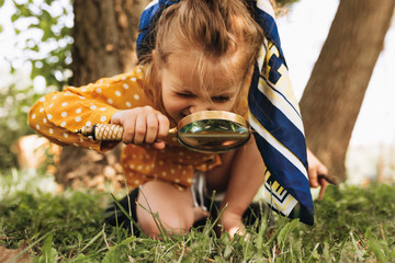 Image of cute kid with magnifying glass exploring the nature outdoors. Adorable little girl playing in the forest with magnifying glass. Curious child looking through magnifier on a sunny day in park