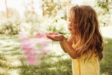 Image of cute blond little girl is playing in the park blowing magical pink dust for an imagination or fairy tale concept. Beautiful child playing with pink powder in the park during her birthday