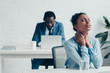 © LIGHTFIELD STUDIOS - selective focus of african american businesswoman suffering from neck pain while sitting near manager working at laptop