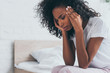 pretty african american woman holding hands near head while suffering from headache in bedroom