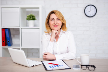 happy mature business woman sitting in office and thinking about something