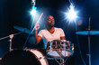 © master1305 - Young african-american jazz musician or drummer playing drums on blue studio background in glowing smoke around him. Concept of music, hobby, inspirness. Colorful portrait of joyful attractive artist.