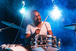 © master1305 - Young african-american jazz musician or drummer playing drums on blue studio background in glowing smoke around him. Concept of music, hobby, inspirness. Colorful portrait of joyful attractive artist.