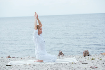 Wall Mural - attractive blonde woman practicing yoga with hands above head near river