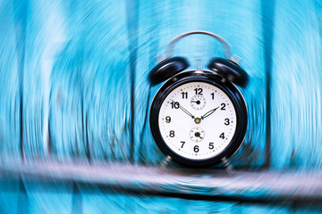 Vintage round shaped alarm clock on the background with blurred motion. Clock hands shown ten to two. Blue wooden wall with rickety boards on the background. Time topic