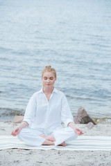 Wall Mural - peaceful blonde young woman with closed eyes practicing yoga near river