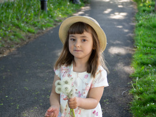 А pretty little girl is picking flowers. A sunny child in a straw hat is picking dandelions on a green glade. Summer girl.